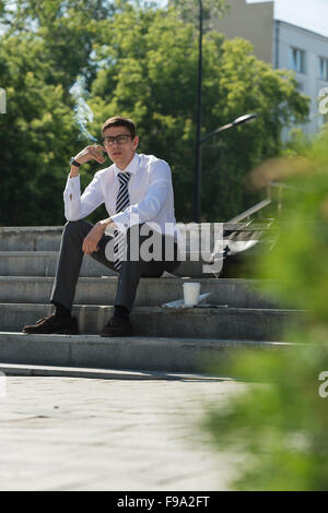 Gut gekleidete Business-Mann Rauchen sitzen auf einer Straße Bürgersteig Stockfoto