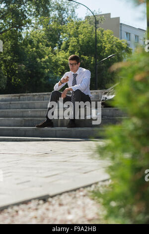 Gut gekleidete Business-Mann Rauchen sitzen auf einer Straße Bürgersteig Stockfoto