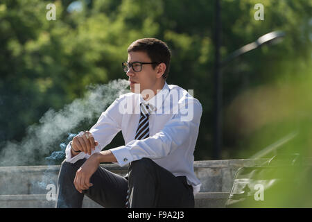 Gut gekleidete Business-Mann Rauchen sitzen auf einer Straße Bürgersteig Stockfoto