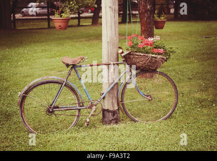 Retro-Stil Bild von einem alten gebrochenen rostigen Fahrrad mit Blumen im Korb Stockfoto