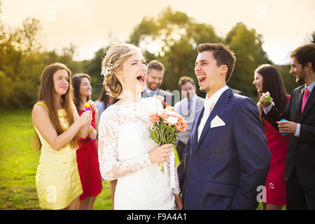 Junge Brautpaar genießen romantische Momente zusammen auf Hochzeit außerhalb, Gäste Hochzeit im Hintergrund Seifenblasen Stockfoto