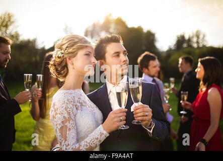 Junge Brautpaar Gläser klirren und genießen romantische Momente zusammen auf Hochzeit außerhalb Stockfoto