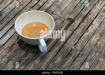 Eine fast overdrunk fertige weiße Tasse Latte Cappuccino Kaffee mit Porzellan Untertasse auf alten Vintage Bambus-Tisch Stockfoto