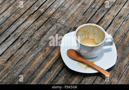 Eine overdrunk fertige weiße Tasse Espresso auf Porzellan Untertasse mit Holzlöffel auf alten Vintage Bambus-Tisch Stockfoto