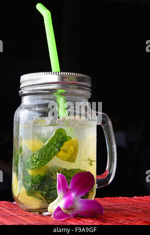 Große Gläser Becher Stil vollen Glas frisch gefrorenen Mojito mit Metallkappe Deckel, Stroh und lila Orchidee Blume im Café mit schwarzen backg Stockfoto