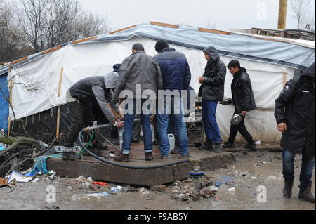 Blick auf die Hälfte gebaut aus Holz Unterschlupf in den überfüllten, schlammigen Bedingungen im Dschungel Flüchtlingslager, Calais. Das Camp ist Heimat von rund 6.000 Menschen und Bedingungen verschlechtern mit dem nassen Wetter. Ansicht von Flüchtlingen sammeln von Wasser aus einem Hahn Stand Rohr. Stockfoto