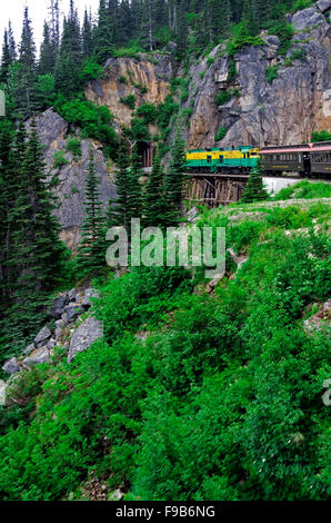 White Pass Railroad Elektromotor zieht Zug Pkw über Trestle Bridge in Richtung Tunnel in den Felsen. Stockfoto