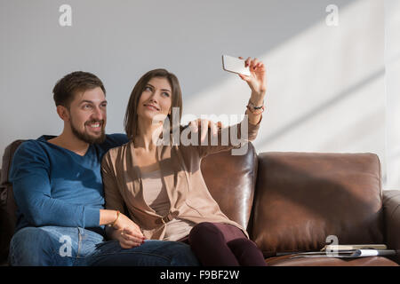 Fröhliches paar die ein Selbstporträt mit einem Smartphone zu Hause sitzen auf couch Stockfoto