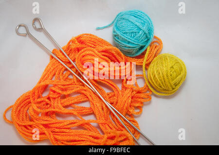 Orange, blue and yellow wool balls and knitting needles on white background Stockfoto