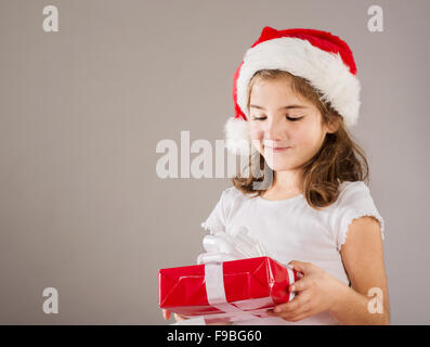 Glückliche kleine Mädchen in Nikolausmütze mit Weihnachtsgeschenk Stockfoto