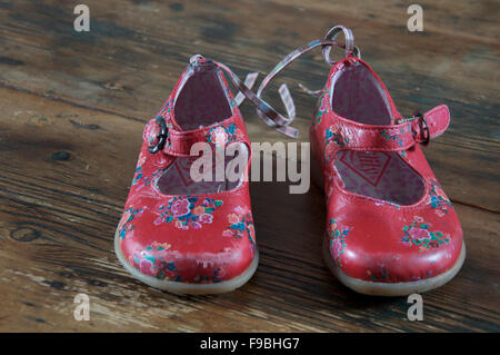 Ein gut getragen paar kleine Mädchen helle rote Schuhe auf einem alten Holzboden gelegt. Stockfoto