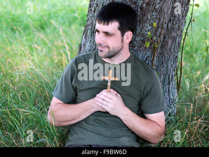 Mann mit Kreuz ist unter Baum beten. Stockfoto