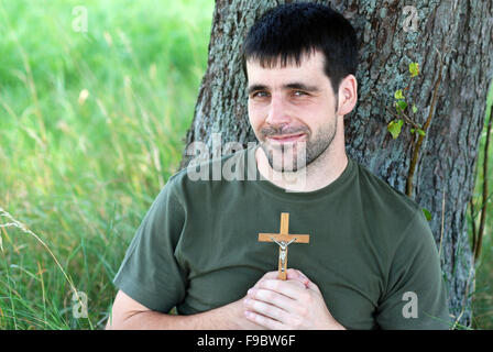 Mann mit Kreuz ist unter Baum beten. Stockfoto