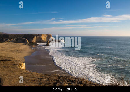 California Klippen mit tiefblauem Himmel und Strähnen von Wolke schäumenden Wogen kaskadiert auf braunen Sandstrand Stockfoto