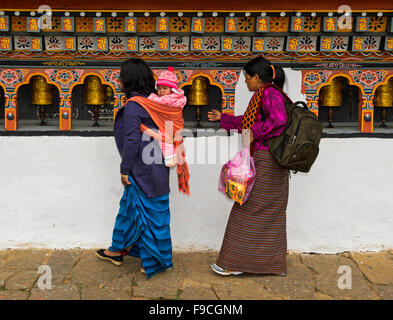 Zwei Frauen mit einem Kleinkind auf dem Rücken drehen Gebet Mühlen, Kloster Chime Lhakhang in der Nähe von Lobesa, Bhutan Stockfoto