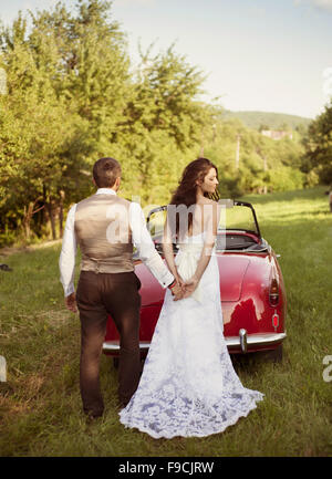 Wunderschöne Braut und Bräutigam Spaß mit roten Retro-Auto in der Natur Stockfoto