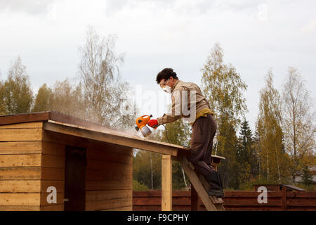 Man malt hölzernen Unterstand mit einer Sprühpistole Stockfoto