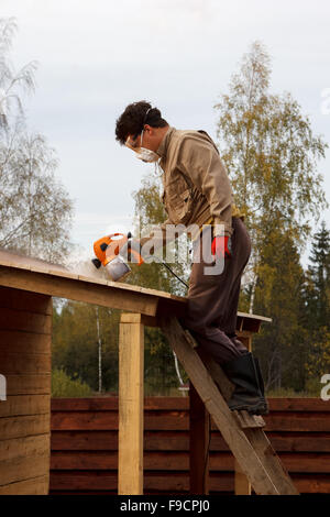 Man malt hölzernen Unterstand mit einer Sprühpistole Stockfoto