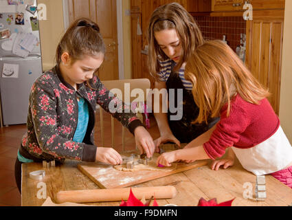 Schneiden den Teig zusammen. Drei Schwestern arbeiten als ein Team um einige Lebkuchenmänner zu Weihnachten zu machen. Stockfoto