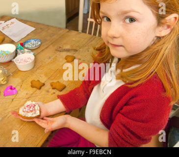 Schau was ich machte. Ein Fünf Jahres altes Mädchen hält ihre Lebkuchen-Kreation mit Zuckerguss verziert und rosa und weißen Candy stars Stockfoto