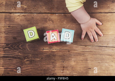 Kleines Baby mit Würfeln mit Papa zu unterzeichnen, auf hölzernen Hintergrund Stockfoto