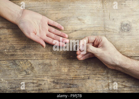 Man bietet einen Ehering zärtlich zu einer Frau. Studio auf einem hölzernen Hintergrund erschossen, Ansicht von oben. Stockfoto