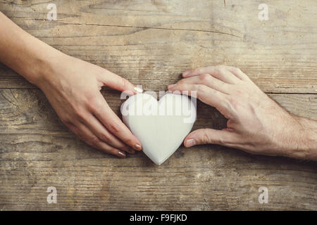 Hände von Mann und Frau durch ein weißes Herz verbunden. Studio auf einem hölzernen Hintergrund erschossen, Ansicht von oben. Stockfoto