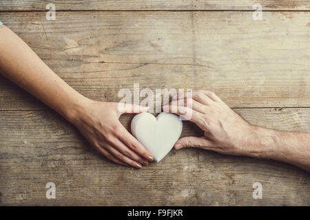 Hände von Mann und Frau durch ein weißes Herz verbunden. Studio auf einem hölzernen Hintergrund erschossen, Ansicht von oben. Stockfoto