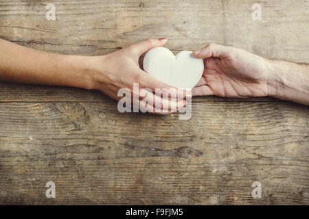 Hände von Mann und Frau durch ein weißes Herz verbunden. Studio auf einem hölzernen Hintergrund erschossen, Ansicht von oben. Stockfoto