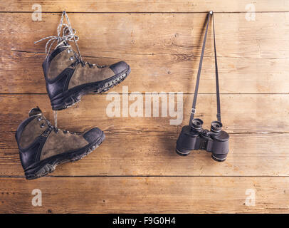 Wanderschuhe und Ferngläser hängen an einem Holzzaun-Hintergrund Stockfoto