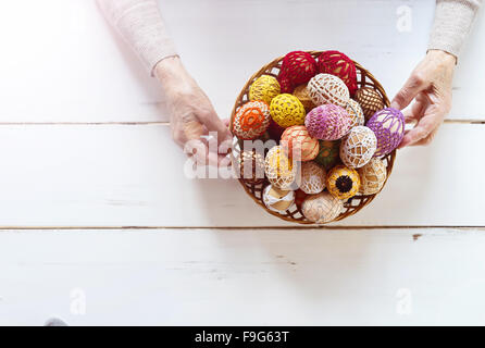 Händen der älteren Frau mit Korb voll von Ostern Eiern auf einem hölzernen weißen Hintergrund. Stockfoto