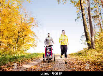 Schöne junge Familie mit Baby im Kinderwagen im Herbst Natur draußen laufen Joggen Stockfoto