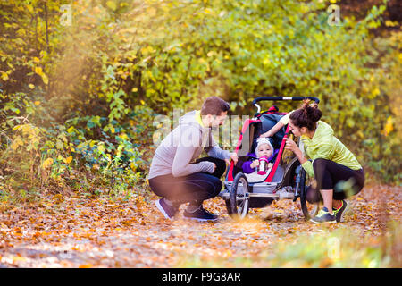 Schöne junge Familie mit Baby im Kinderwagen im Herbst Natur draußen laufen Joggen Stockfoto