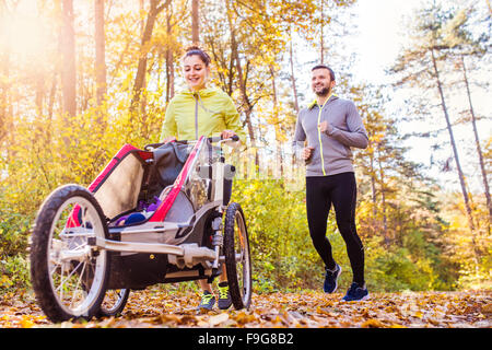 Schöne junge Familie mit Baby im Kinderwagen im Herbst Natur draußen laufen Joggen Stockfoto