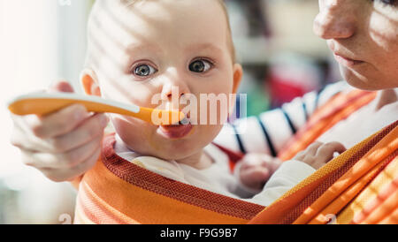 Junge Mutter füttert ihre kleine Tochter, die sie in einem Tragetuch hat Stockfoto