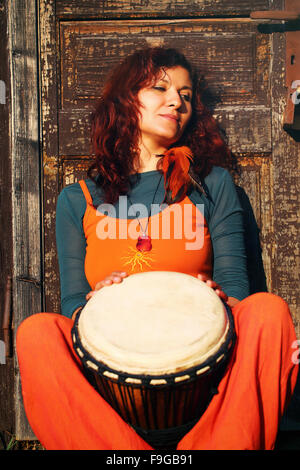 Junge Dame Schlagzeuger mit ihrer Djembe-Trommel auf rustikale Holztür Hintergrund. Stockfoto