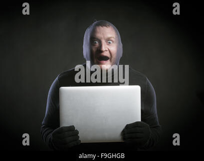 Dieb in Aktion mit Sturmhaube auf seinem Gesicht, in schwarz gekleidet. Studio auf schwarzem Hintergrund gedreht. Stockfoto
