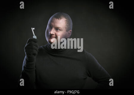 Dieb in Aktion mit Sturmhaube auf seinem Gesicht, in schwarz gekleidet. Studio auf schwarzem Hintergrund gedreht. Stockfoto