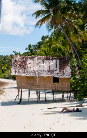 Einsame Nipa-Hütte auf Stelzen mit Palmen Bäume an einem schönen Strand vor auf das Meer und die Person Sonnenbaden Stockfoto