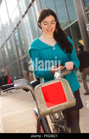 junge Frau mit einem Mietwagen Fahrrad überprüft ihr Telefon Stockfoto