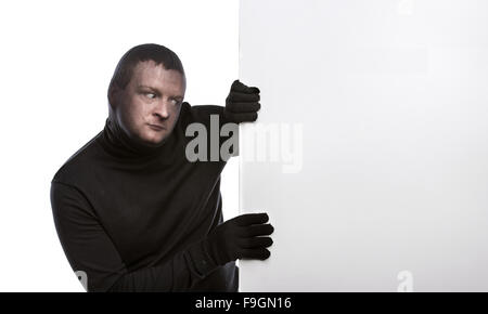 Dieb mit Sturmhaube auf seinem Gesicht, in schwarz gekleidet, hält einen leere Banner. Studio auf weißem Hintergrund gedreht. Stockfoto