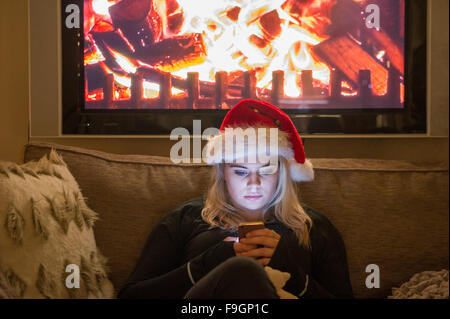 Ein hübsches junges Mädchen nutzt ihr Handy in der Dunkelheit, während eine Weihnachtsmütze tragen Stockfoto