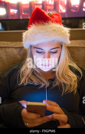 Ein hübsches junges Mädchen nutzt ihr Handy in der Dunkelheit, während eine Weihnachtsmütze tragen Stockfoto