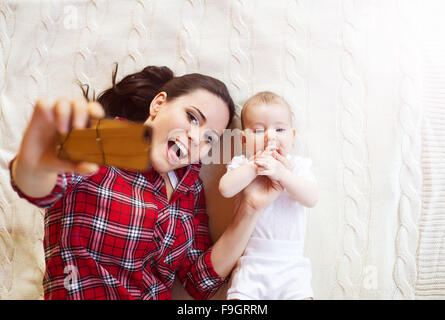 Niedliche kleine Baby-Mädchen und ihre Mutter nehmen Selfie auf einer Decke im Wohnzimmer. Stockfoto