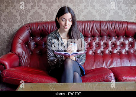 junge Frau, die ein Buch mit einem Getränk Stockfoto