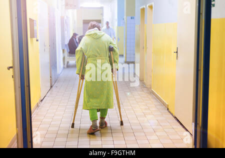 Ältere Frau verletzt sitzen auf dem Flur des Krankenhauses mit Krücken Stockfoto