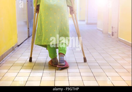 Ältere Frau verletzt sitzen auf dem Flur des Krankenhauses mit Krücken Stockfoto