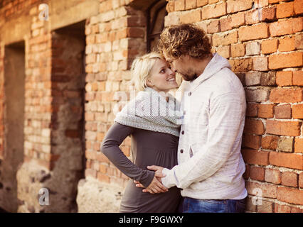 Glückliche junge schwangere paar vor einem alten Backsteinhaus stehen. Stockfoto