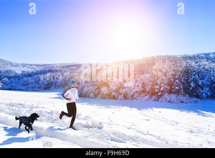 Junge Sportler Joggen mit Hund draußen im sonnigen Winter park Stockfoto