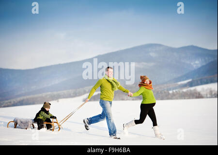 Glückliche Eltern mit ihrem Sohn auf Schlitten Spaß draußen in den Schnee fahren. Stockfoto